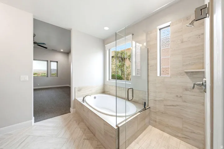 Soaking tub with a tiled surround, framed by a glass-enclosed shower