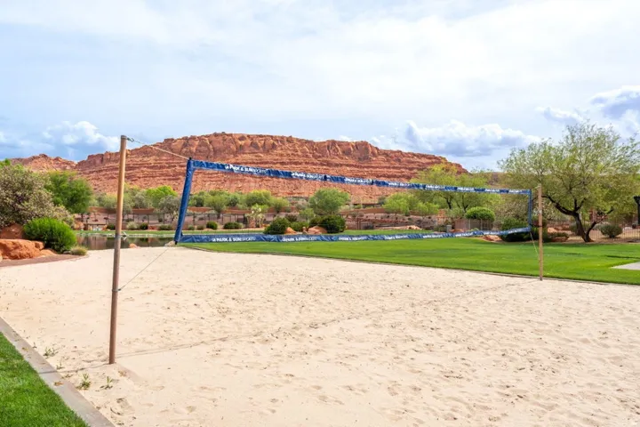 Sand volleyball court featuring a net, adjacent to a manicured lawn and mature trees