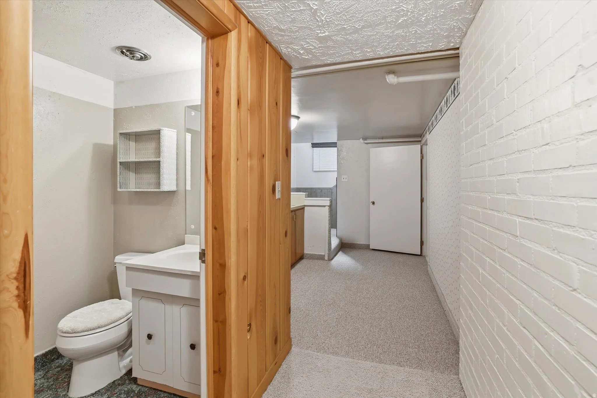 Hardwood paneling defining a bathroom entry with a white vanity, toilet, and mounted shelving