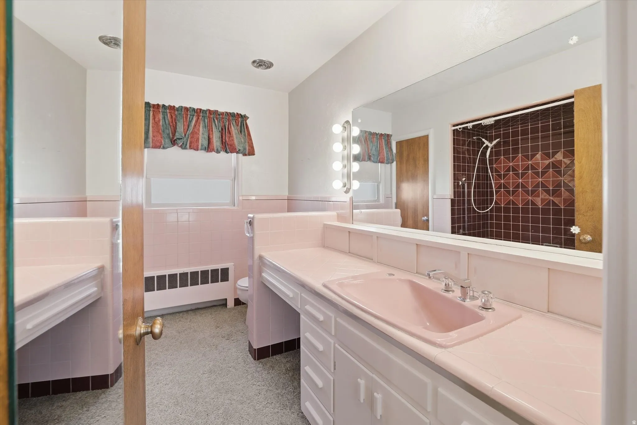 Bathroom featuring a vanity with a pink ceramic sink, extensive countertop space, multiple lower cabinets, and a large wall-mounted mirror