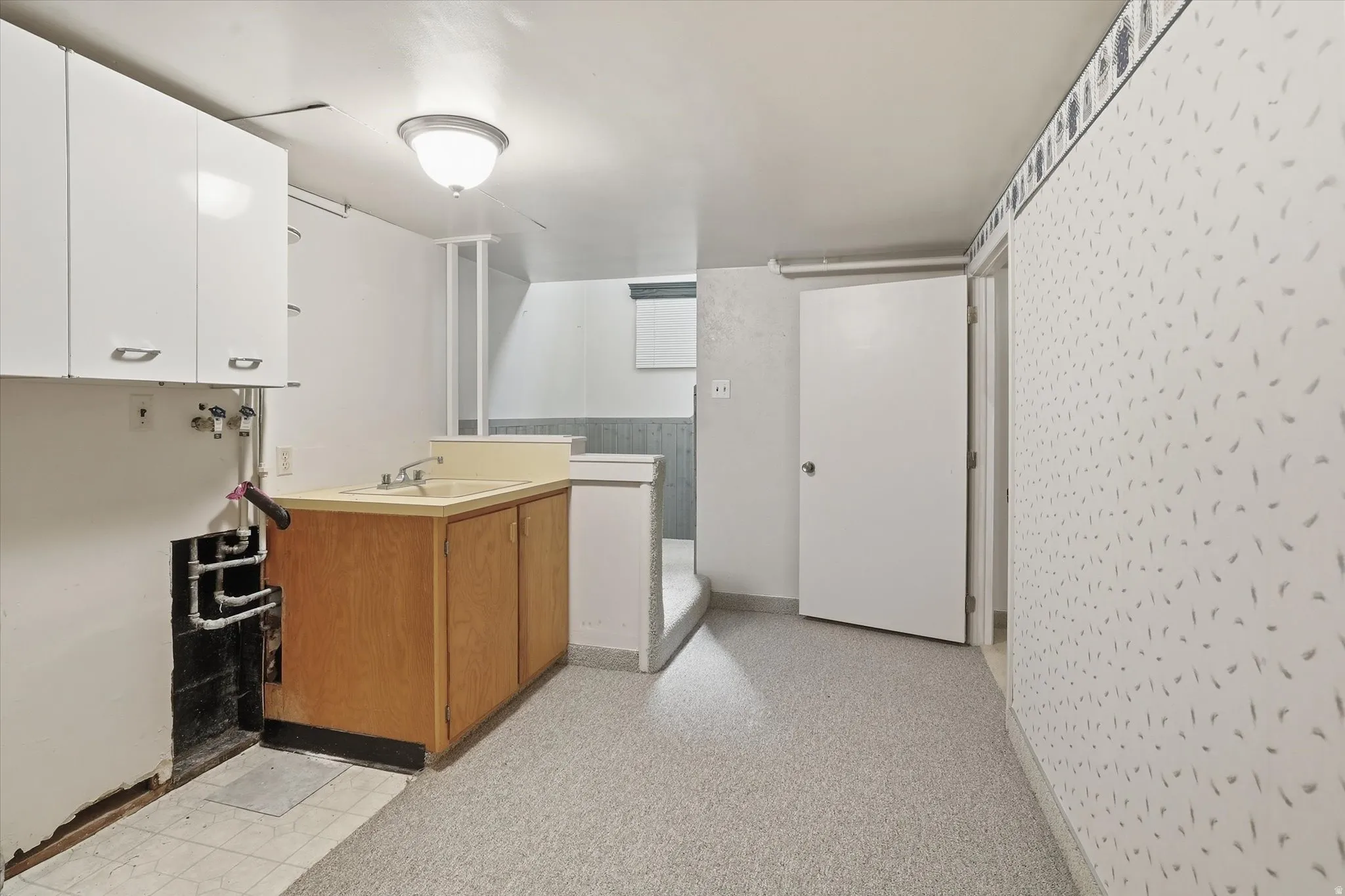 Utility area featuring a built-in sink with a wooden base cabinet, overhead white cabinetry, and light-colored flooring