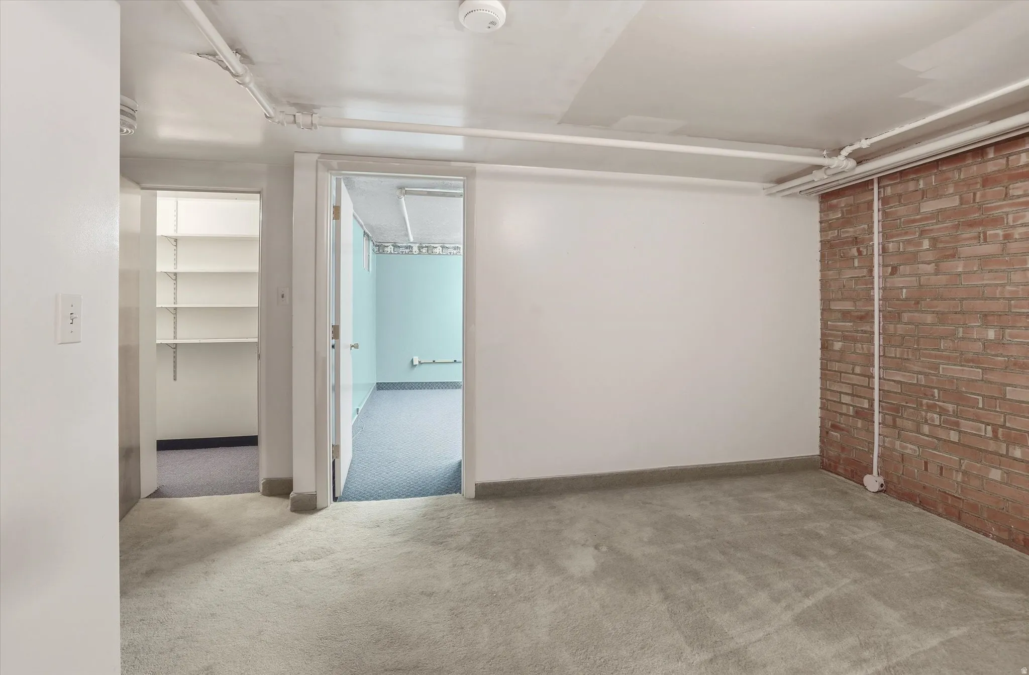 Expansive room featuring light gray carpet, exposed brick accent wall, and painted white ceiling
