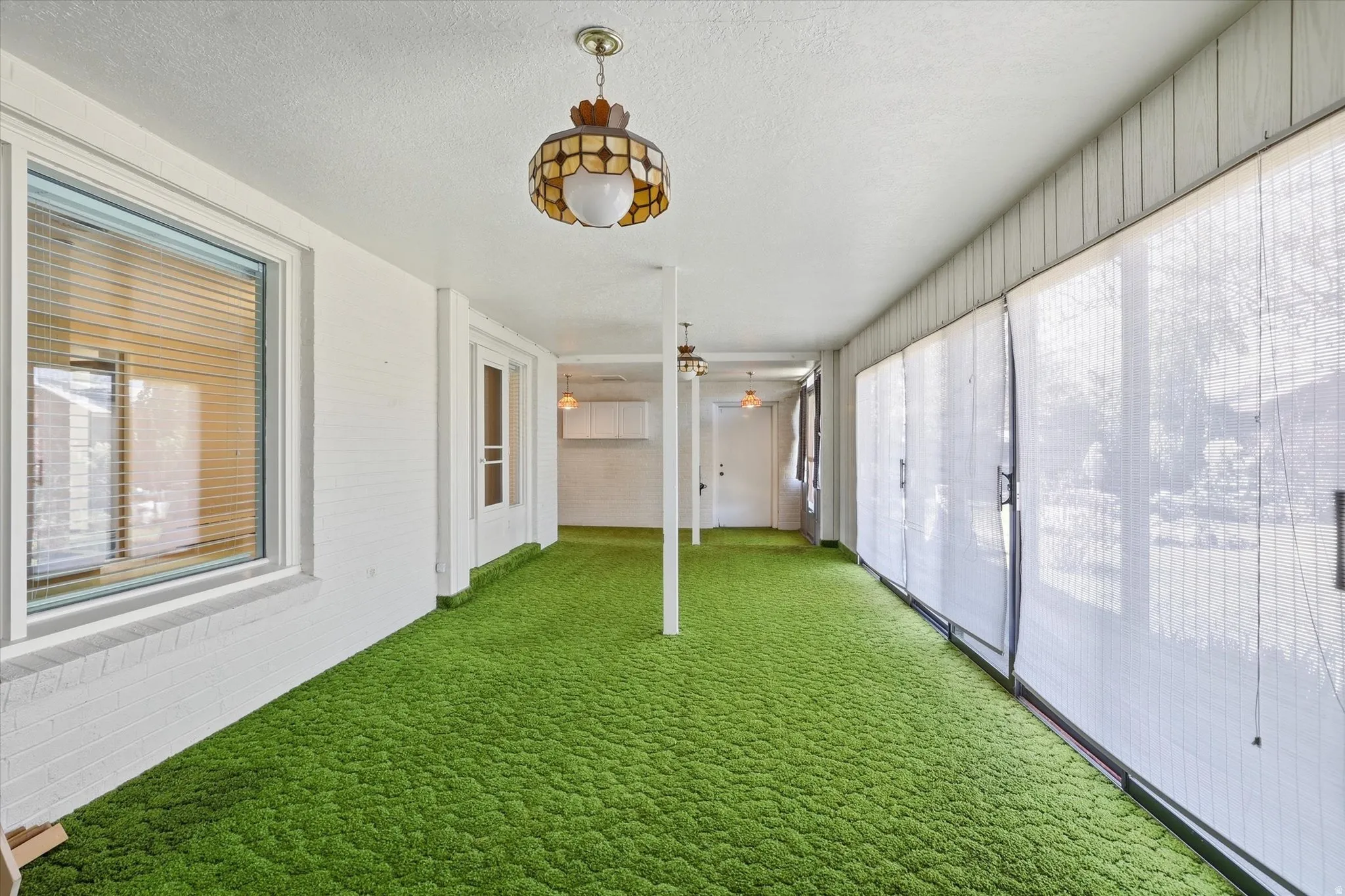 Enclosed patio featuring green low-pile carpet, white brick wall, white paneling, and multiple pendant light fixtures