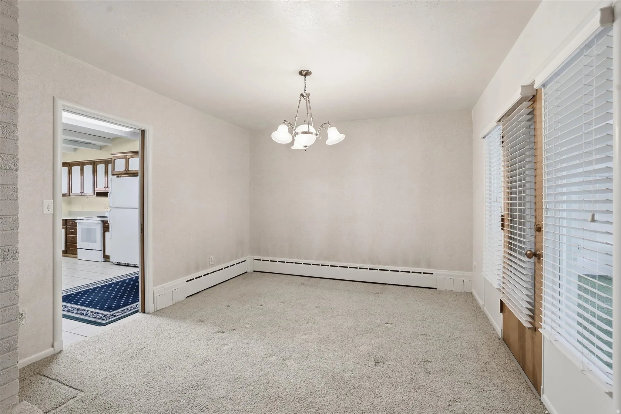 Carpeted room with a multi-light ceiling fixture, baseboard heating, and sliding glass doors with blinds