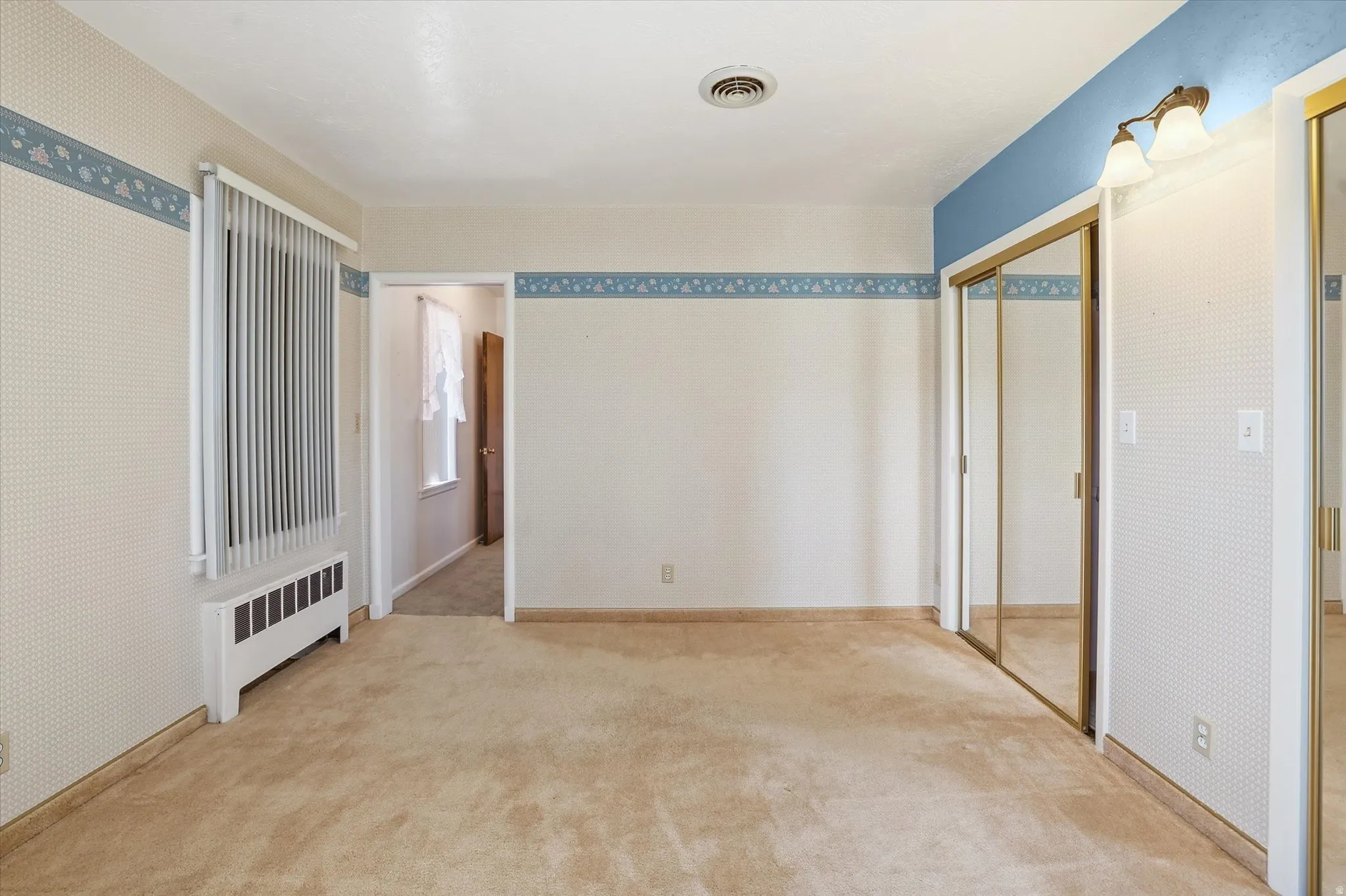 Carpeted room featuring a window with vertical blinds, a baseboard heating unit, and mirrored closet doors