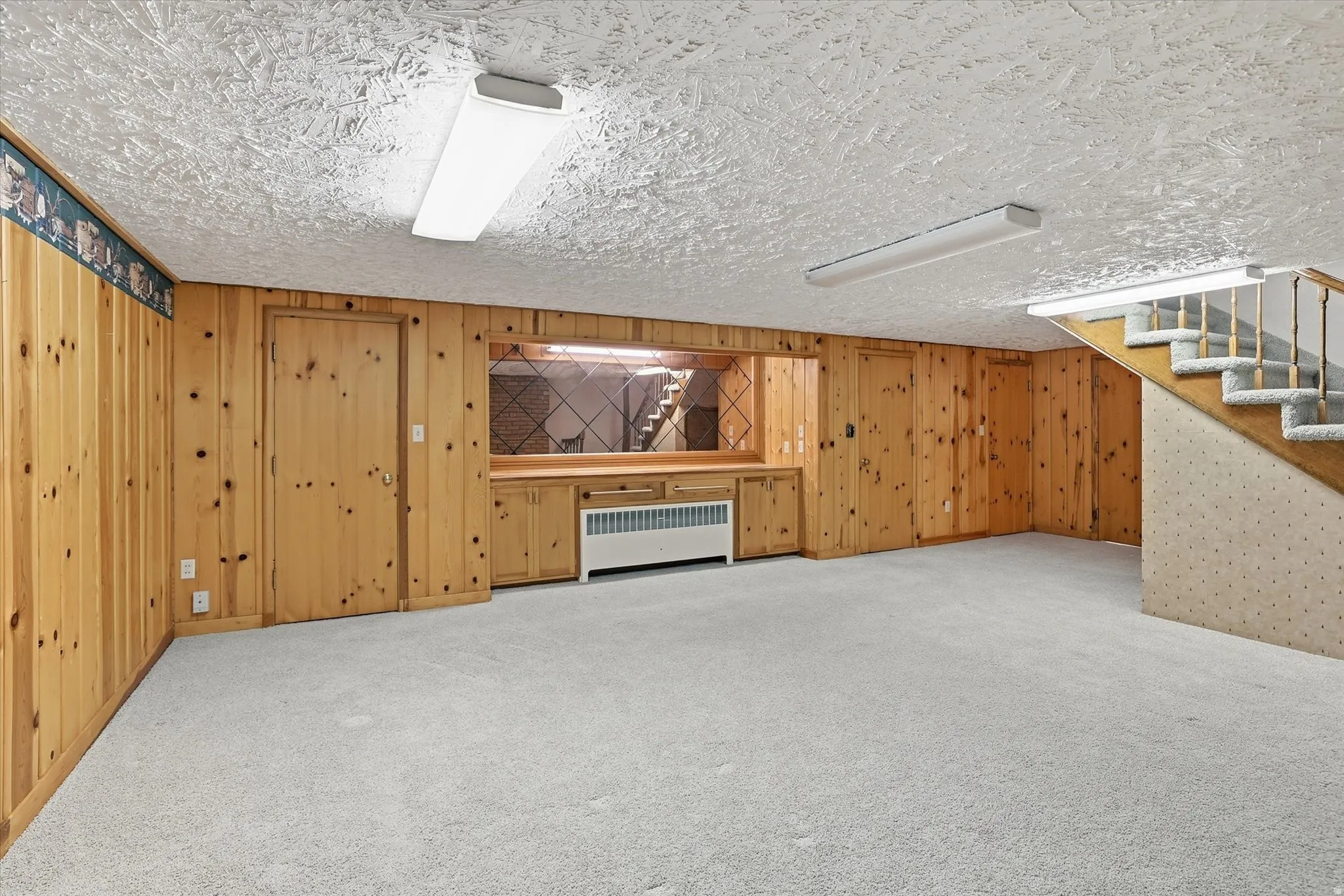 Spacious room featuring light wood paneling, light-toned carpeting, and a built-in counter with mirrored accents