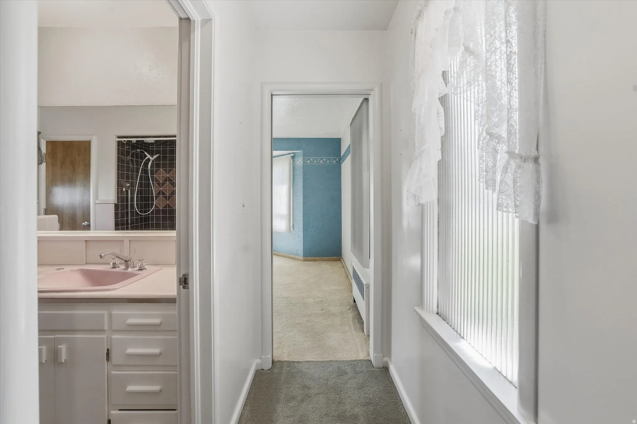 Hallway with carpet flooring and white walls, featuring a window with vertical blinds