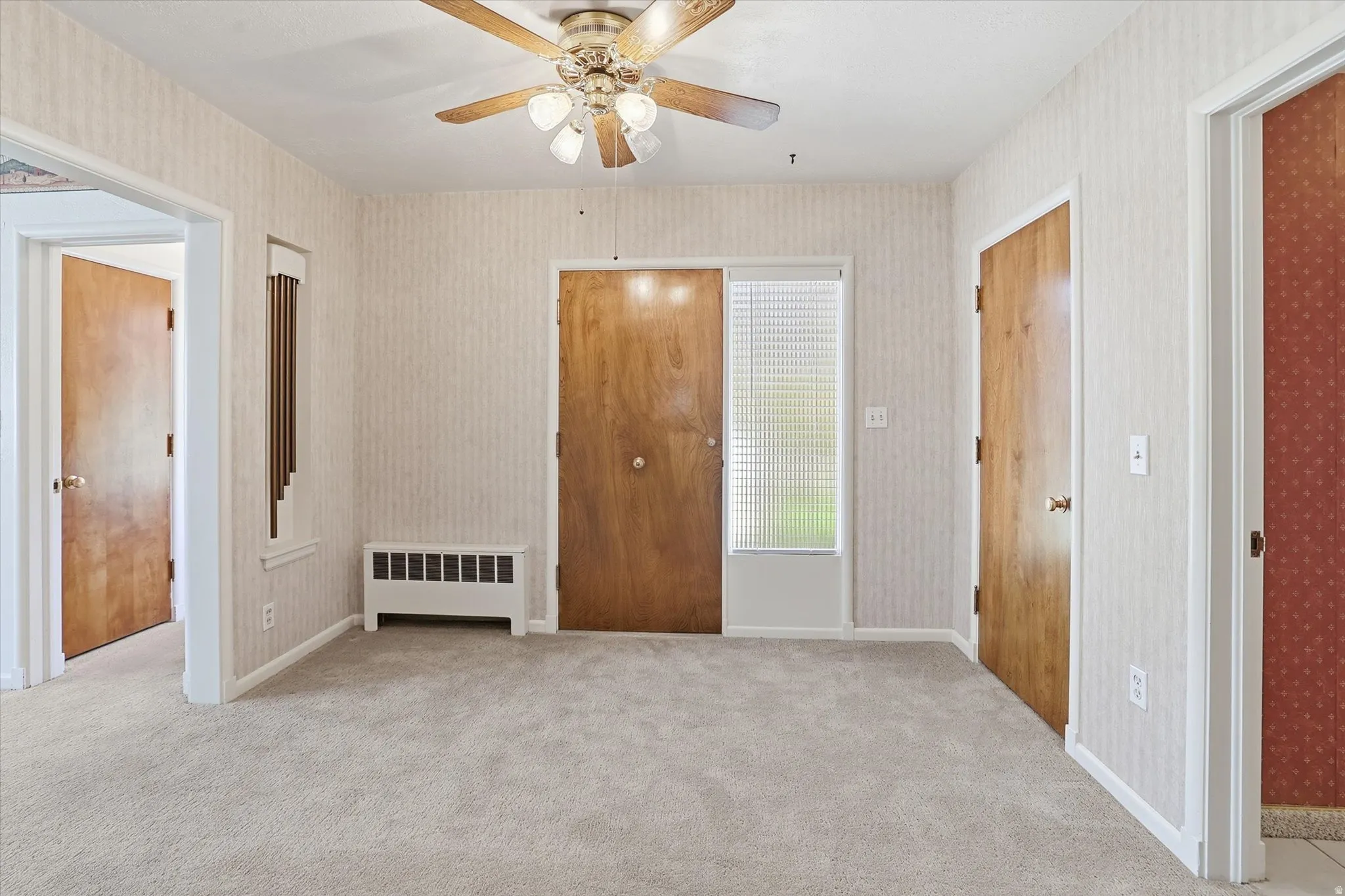 Carpeted interior space featuring a ceiling fan, multiple wooden doors, and a window with blinds
