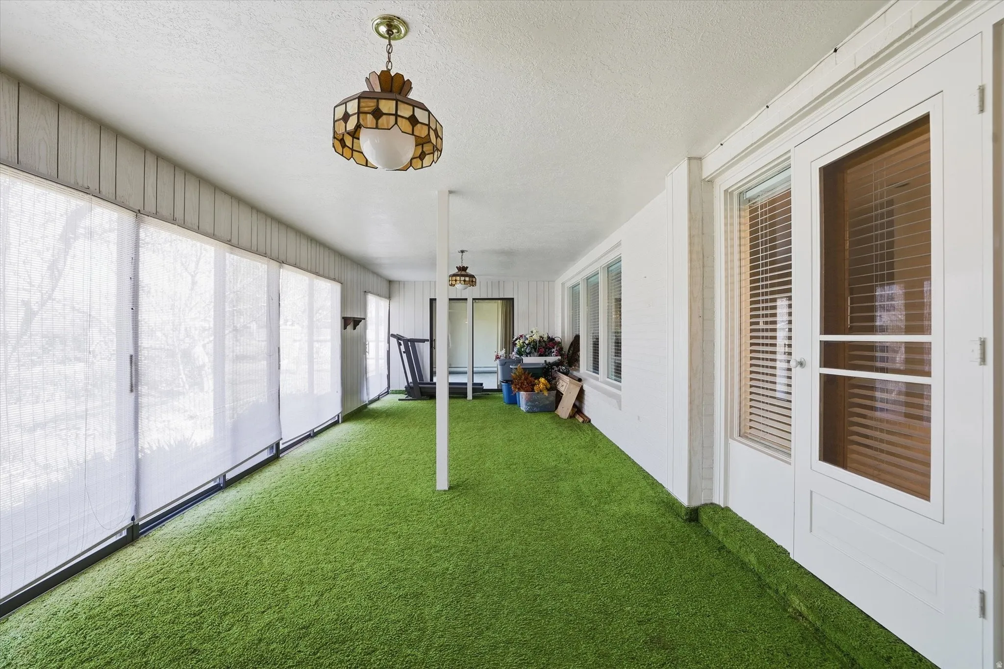 Enclosed patio featuring artificial turf flooring and a full wall of floor-to-ceiling windows with privacy shades