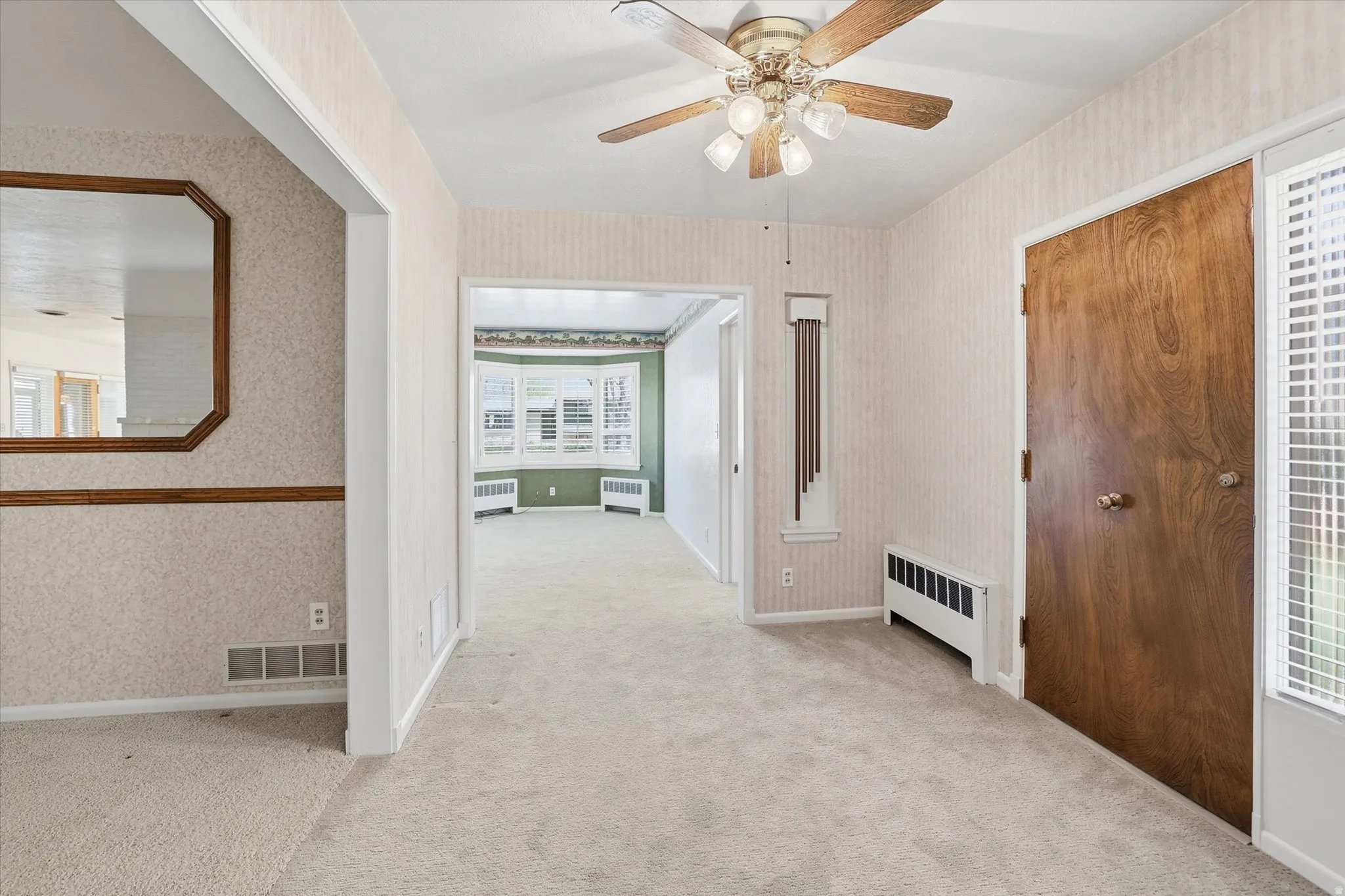 Carpeted interior entryway featuring a ceiling fan with integrated lighting, wood-paneled door, and an octagonal wall mirror