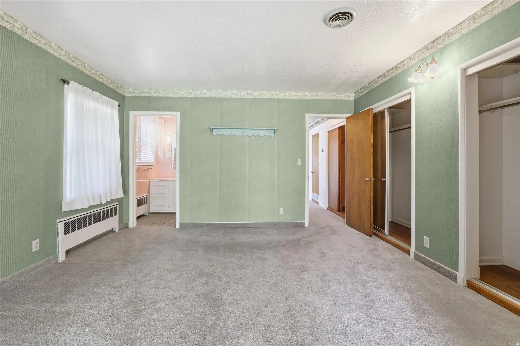Carpeted room featuring textured green wallpaper, white trim, and a window with a radiator