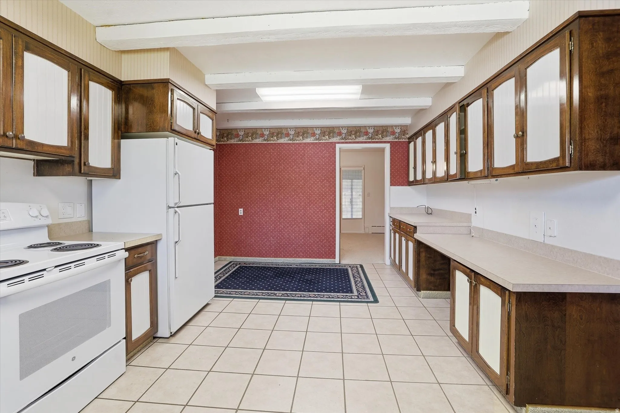 Spacious kitchen featuring white tile flooring, extensive wood cabinetry with frosted glass inserts, and light-toned countertops