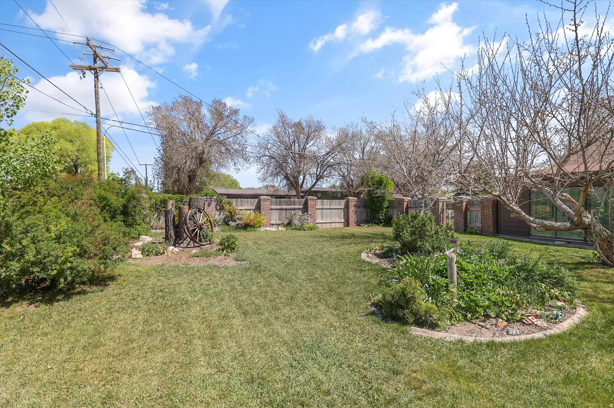 Expansive backyard featuring a manicured lawn, established garden beds with brick edging, a wood and brick perimeter fence, and mature trees