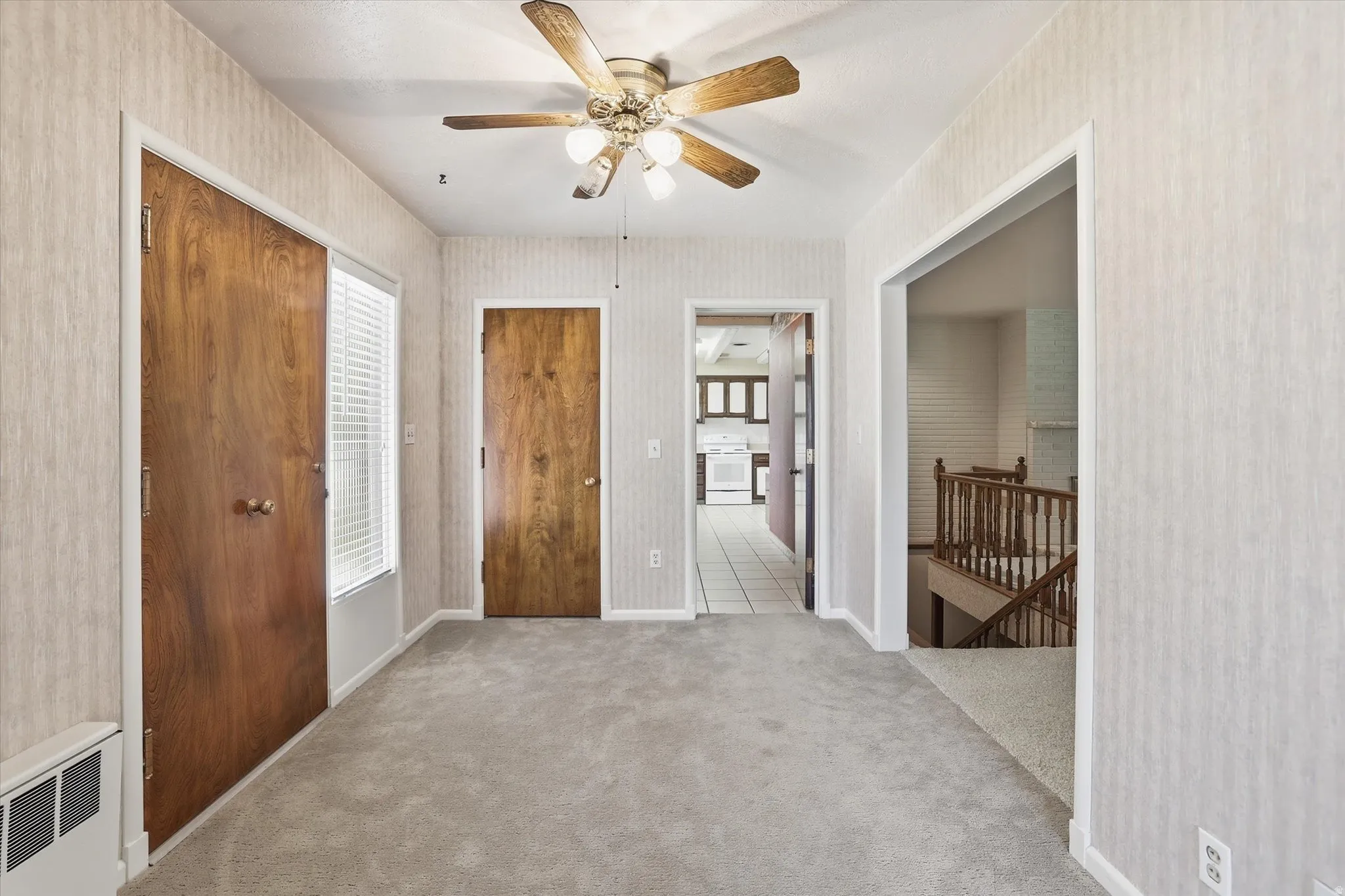 Carpeted room featuring a ceiling fan with light fixture, light-toned patterned wallpaper, and wood-panel doors