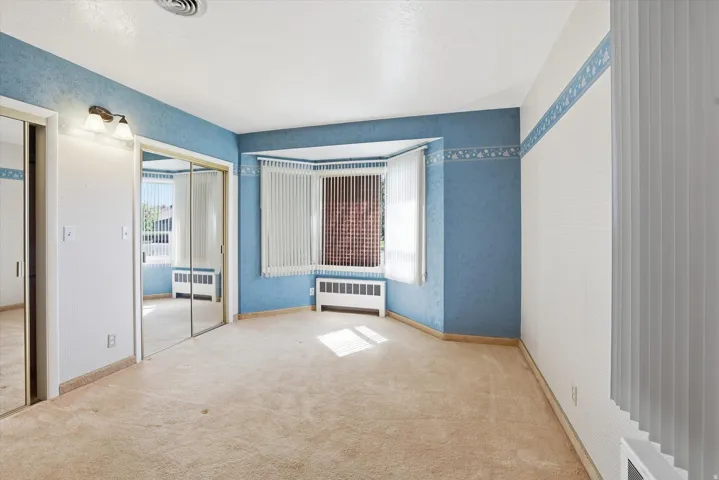 Carpeted room featuring a bay window with vertical blinds, wall-mounted lighting fixture, and mirrored closet doors
