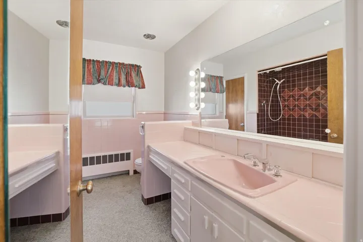 Bathroom featuring a vanity with a pink ceramic sink, extensive countertop space, multiple lower cabinets, and a large wall-mounted mirror