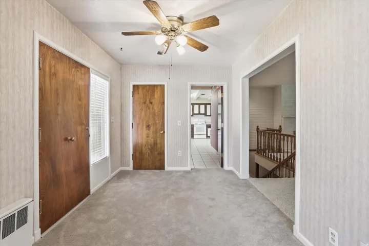 Carpeted room featuring a ceiling fan with light fixture, light-toned patterned wallpaper, and wood-panel doors