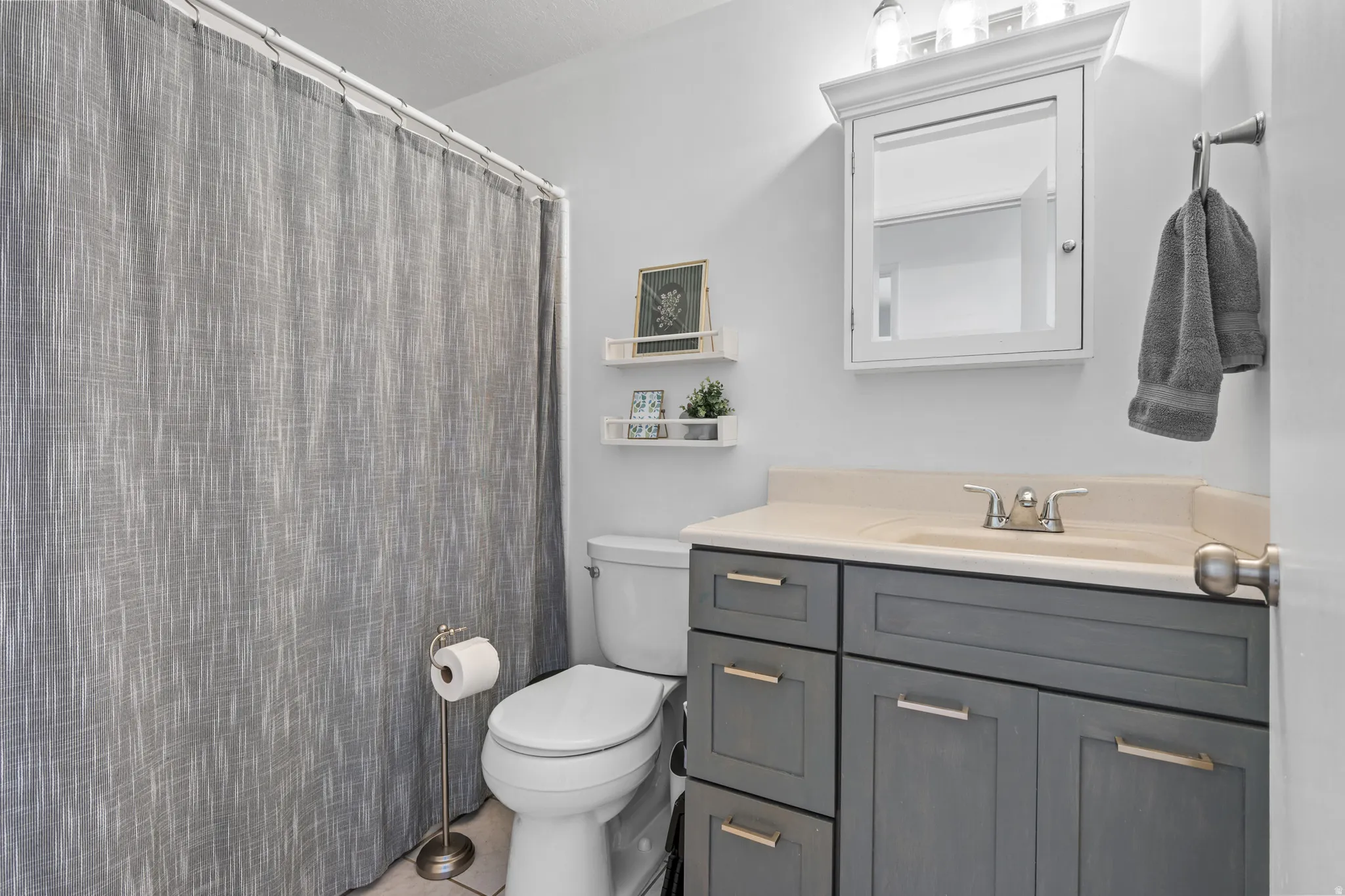 Bathroom featuring a gray vanity with gold-tone hardware, a white countertop, and an integrated sink