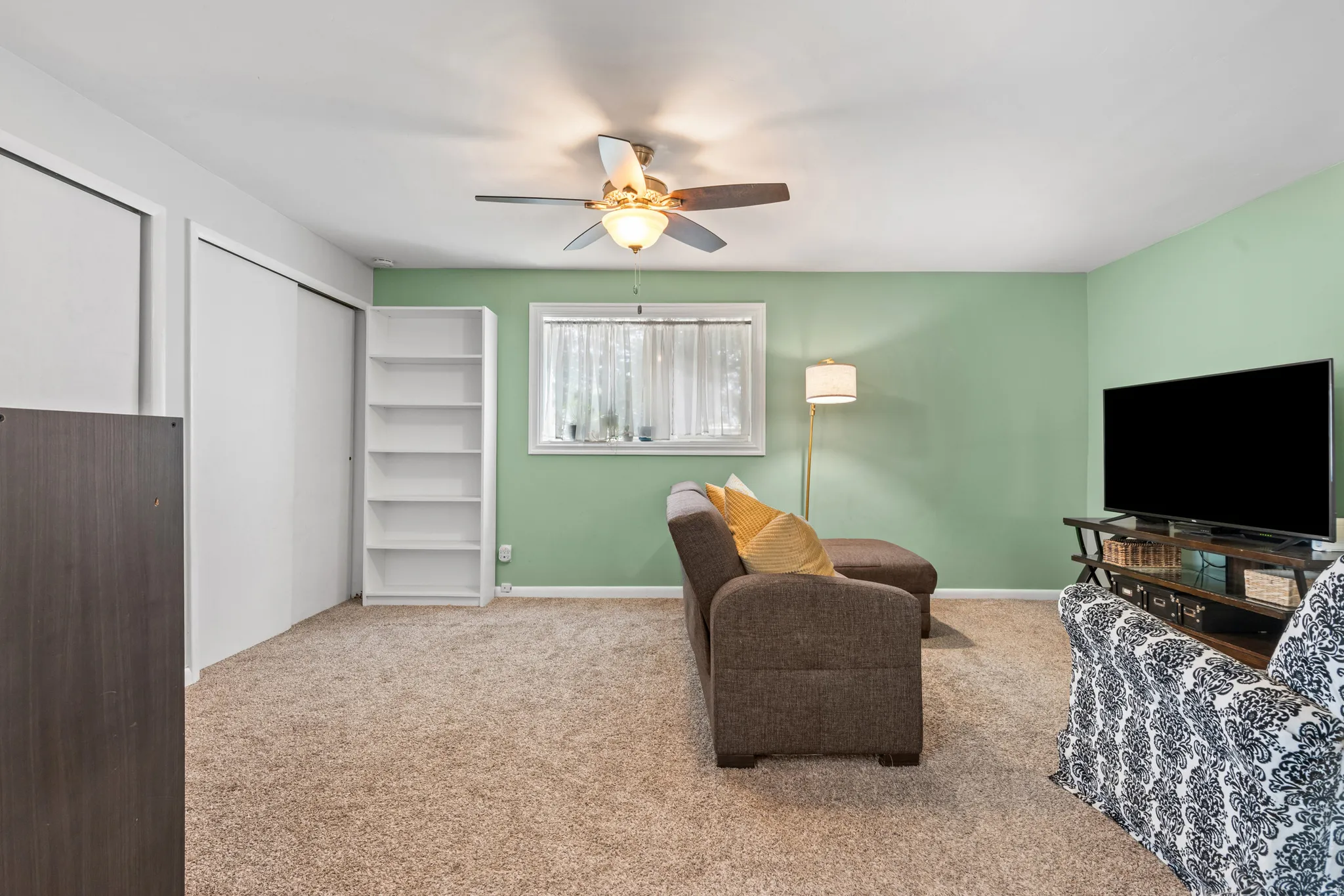 Carpeted room featuring a ceiling fan with integrated lighting, a window with white trim, and a built-in white bookshelf