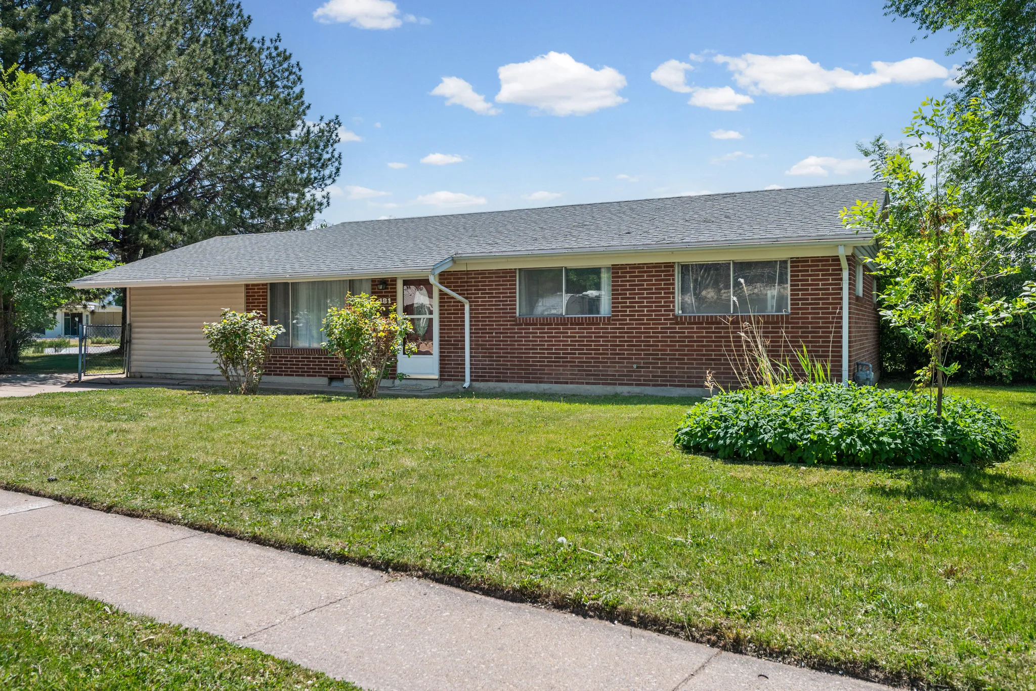 Brick and siding exterior featuring a gray shingle roof, well-maintained front lawn, mature trees, and a concrete sidewalk