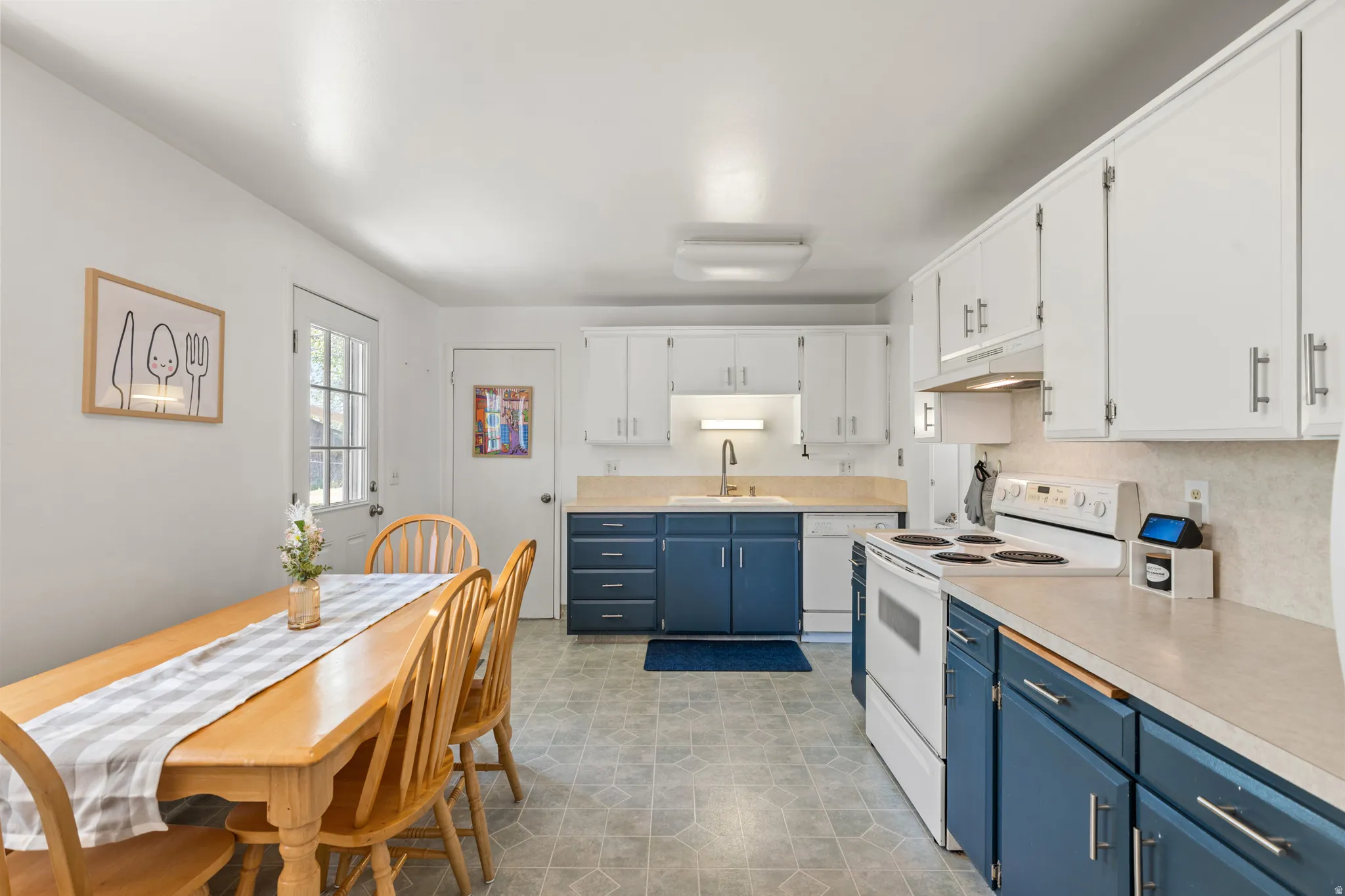 Kitchen featuring white upper cabinetry, blue lower cabinetry, light-toned countertops, and vinyl flooring