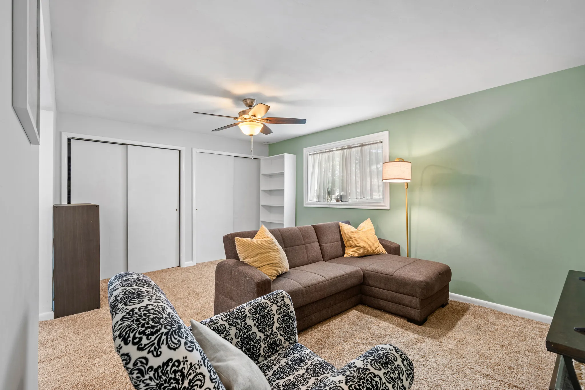 Carpeted room featuring a ceiling fan with integrated lighting, a window with natural light, and two large sliding closet doors