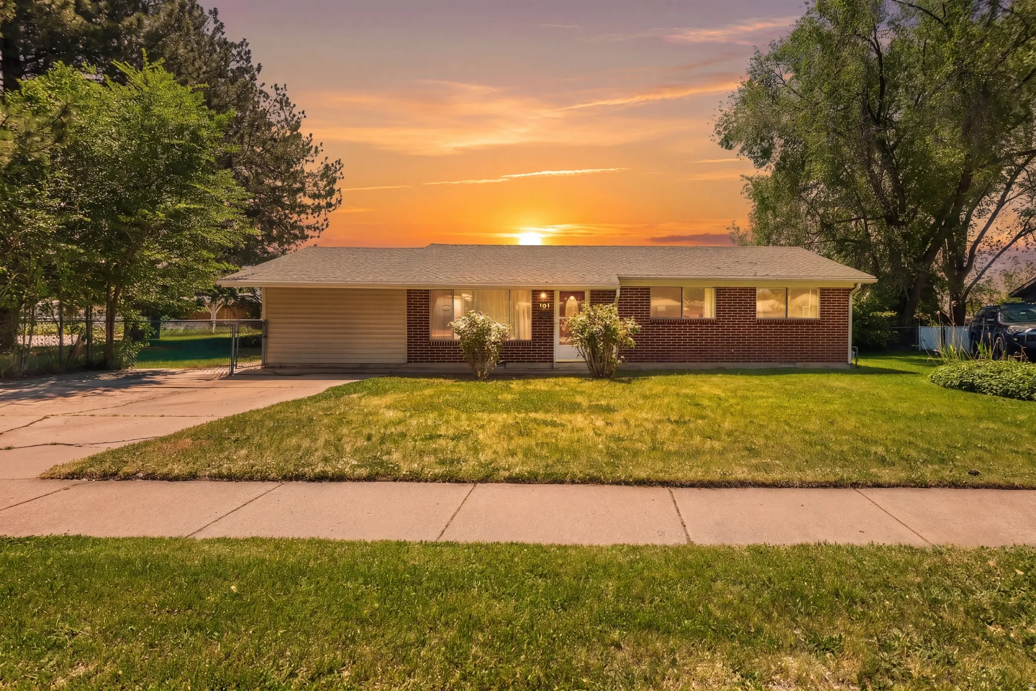 Ranch-style exterior featuring brick and vinyl siding, a well-maintained lawn, mature trees, and a concrete driveway