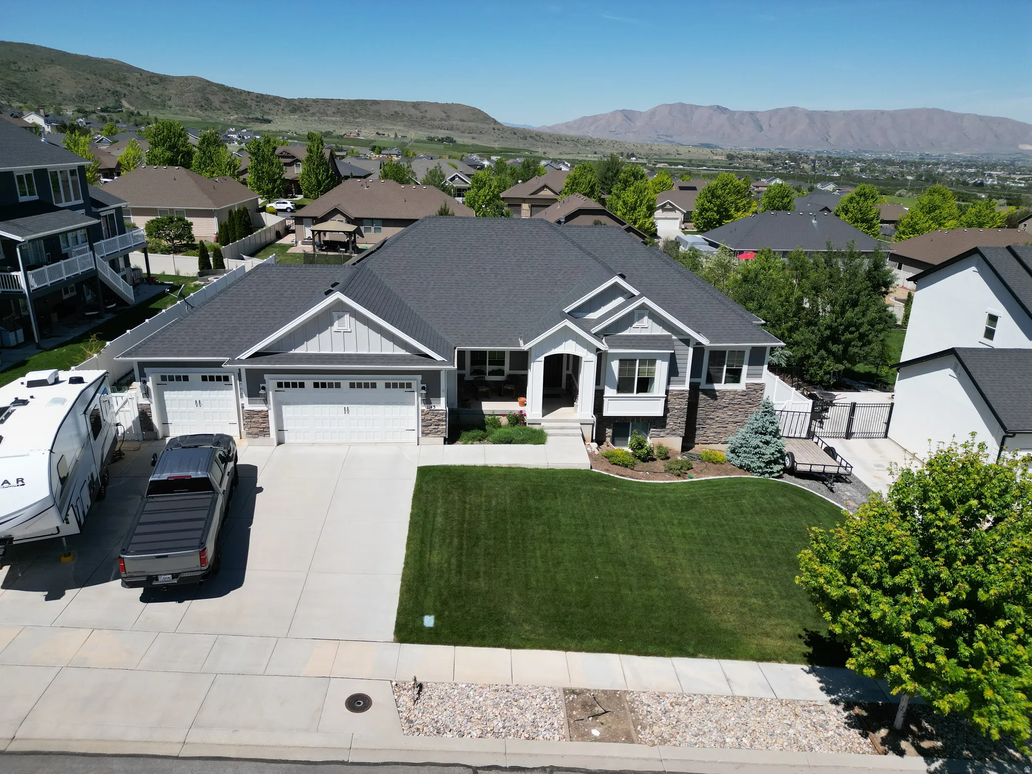 Modern American Craftsman exterior featuring a dark gray asphalt shingle roof, light gray siding, stone accents, and a landscaped front yard with a green lawn