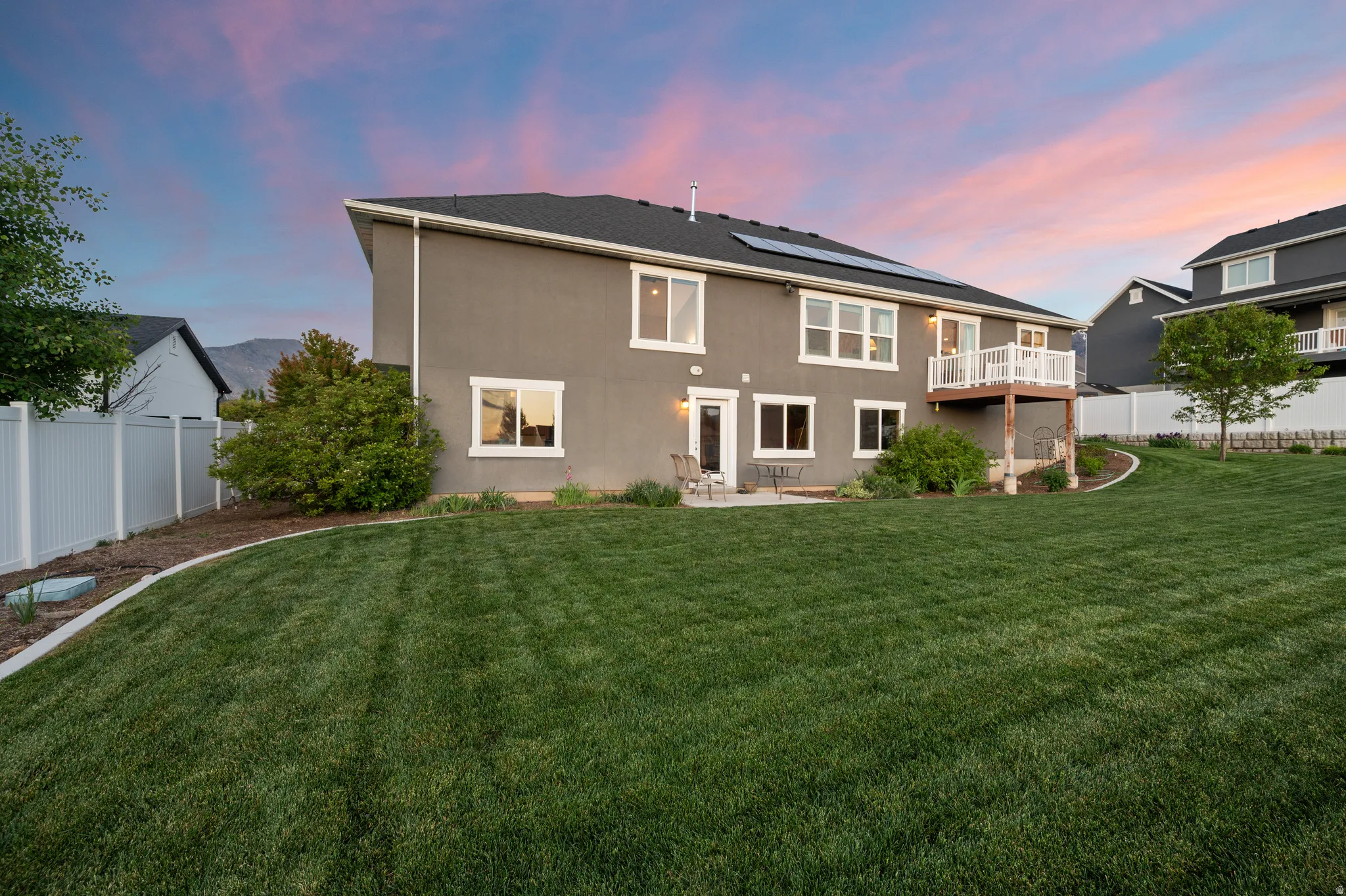 Expansive backyard featuring a large green lawn, concrete patio, and upper-level deck with white railing