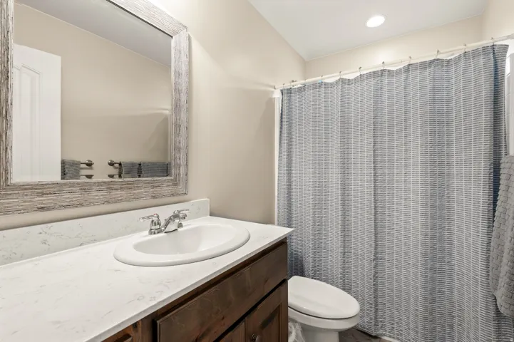 Bathroom featuring a wood-finish vanity with an integrated sink and light-toned countertop, a decorative mirror with a distressed frame, a toilet, and a shower area
