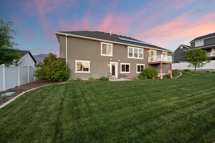 Expansive backyard featuring a large green lawn, concrete patio, and upper-level deck with white railing