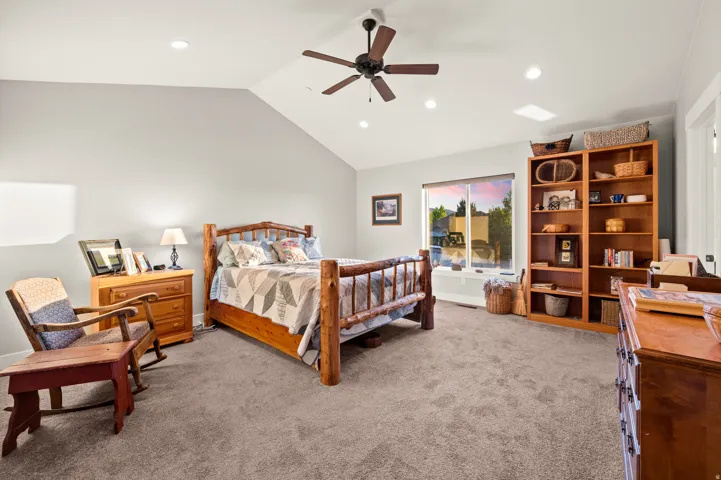 Spacious master bedroom featuring vaulted ceilings, recessed lighting, a ceiling fan, a large window, and built-in shelving