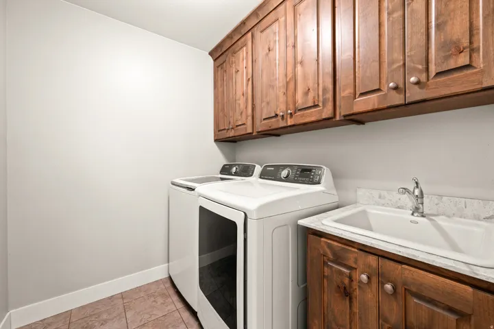 Laundry area featuring wood-finish cabinetry, a utility sink with a stone-finish countertop, and tile flooring