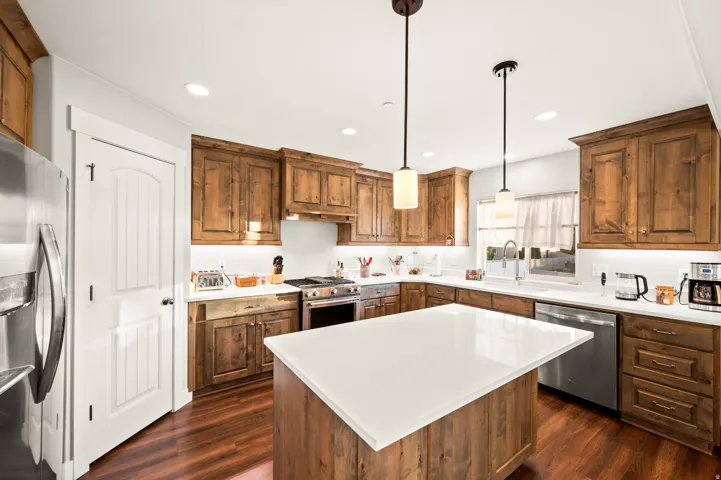 Spacious kitchen featuring a large central island with a white solid surface countertop, wood-finish flooring, full-height wood cabinetry, stainless steel appliances, and recessed lighting