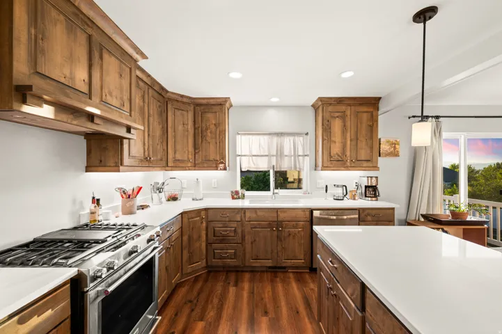 Expansive kitchen featuring wood-finish cabinetry, white countertops, built-in stainless steel appliances, wood-finish flooring, and recessed lighting