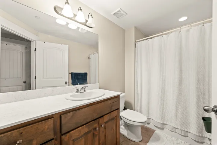 Spacious bathroom featuring an oval undermount sink set into a light-toned countertop, a wood-finish vanity with cabinet storage, a wide mirror, and an overhead light bar
