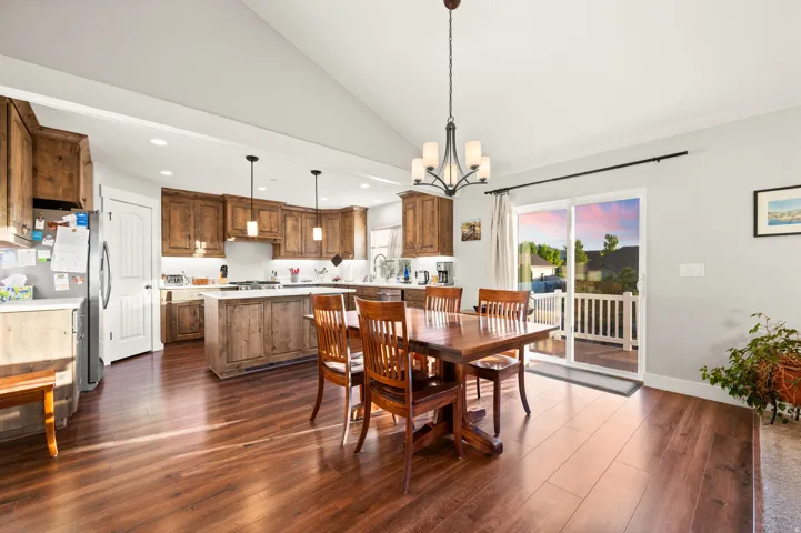 Open-concept kitchen and dining area featuring wood-finish flooring, vaulted ceilings, and a sliding glass door to an exterior deck