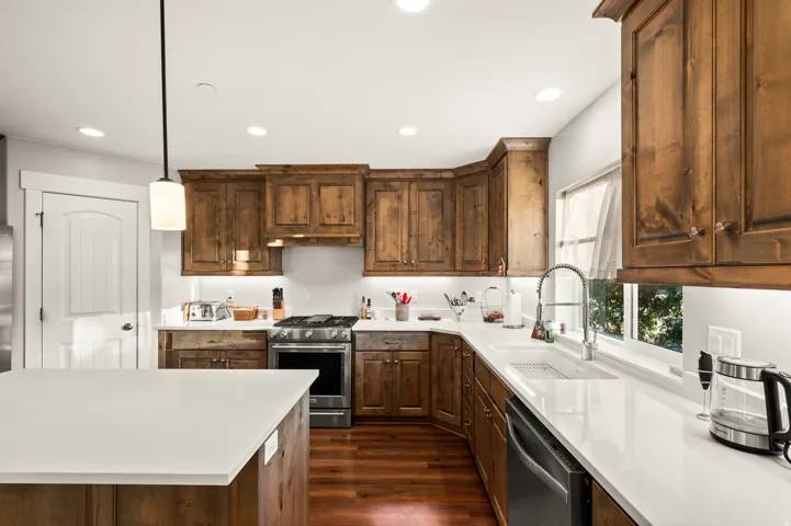 Spacious kitchen featuring extensive wood cabinetry, white countertops, stainless steel appliances, and wood-finish flooring