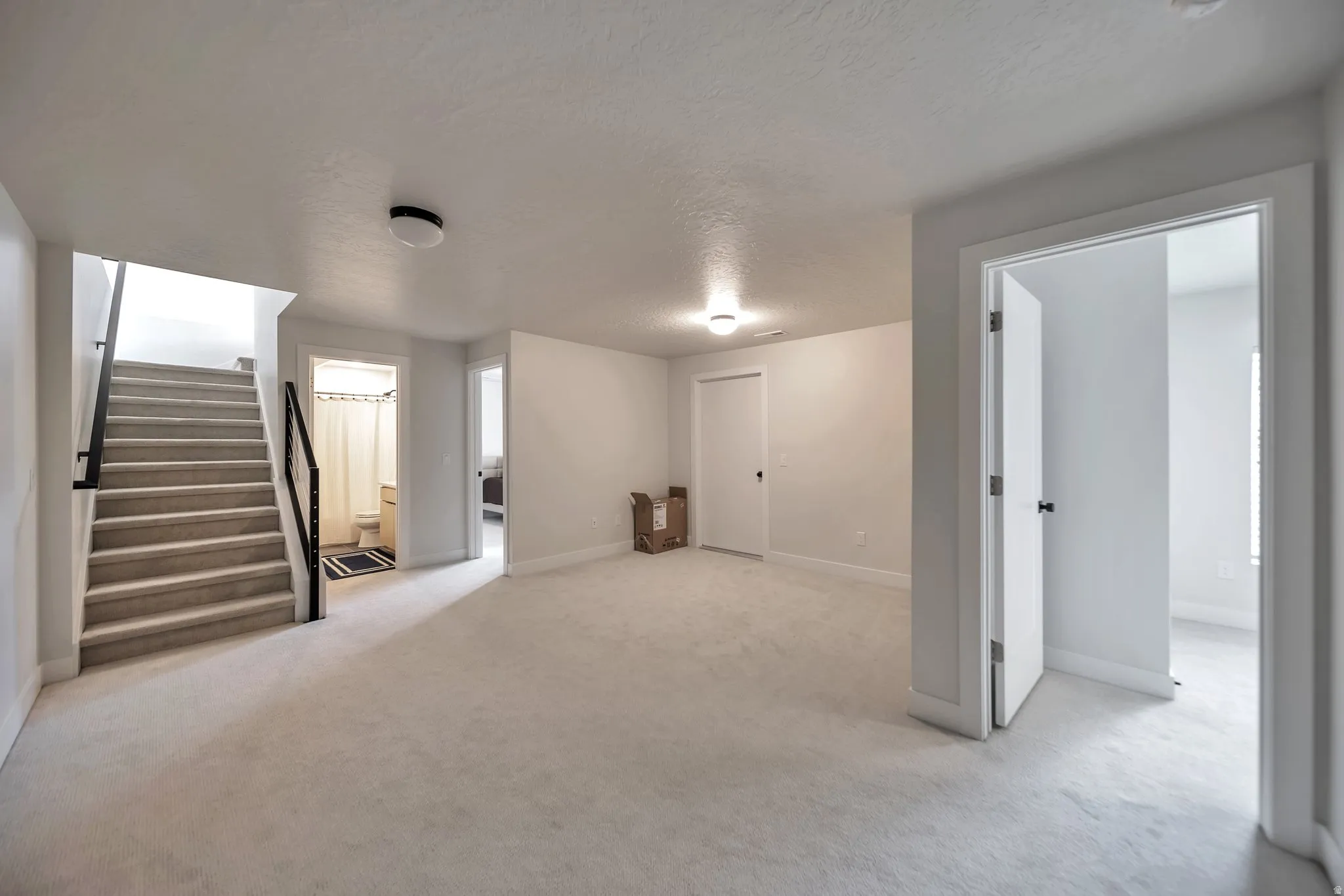 Carpeted open area featuring a staircase with black metal railings, white walls, and flush-mount lighting
