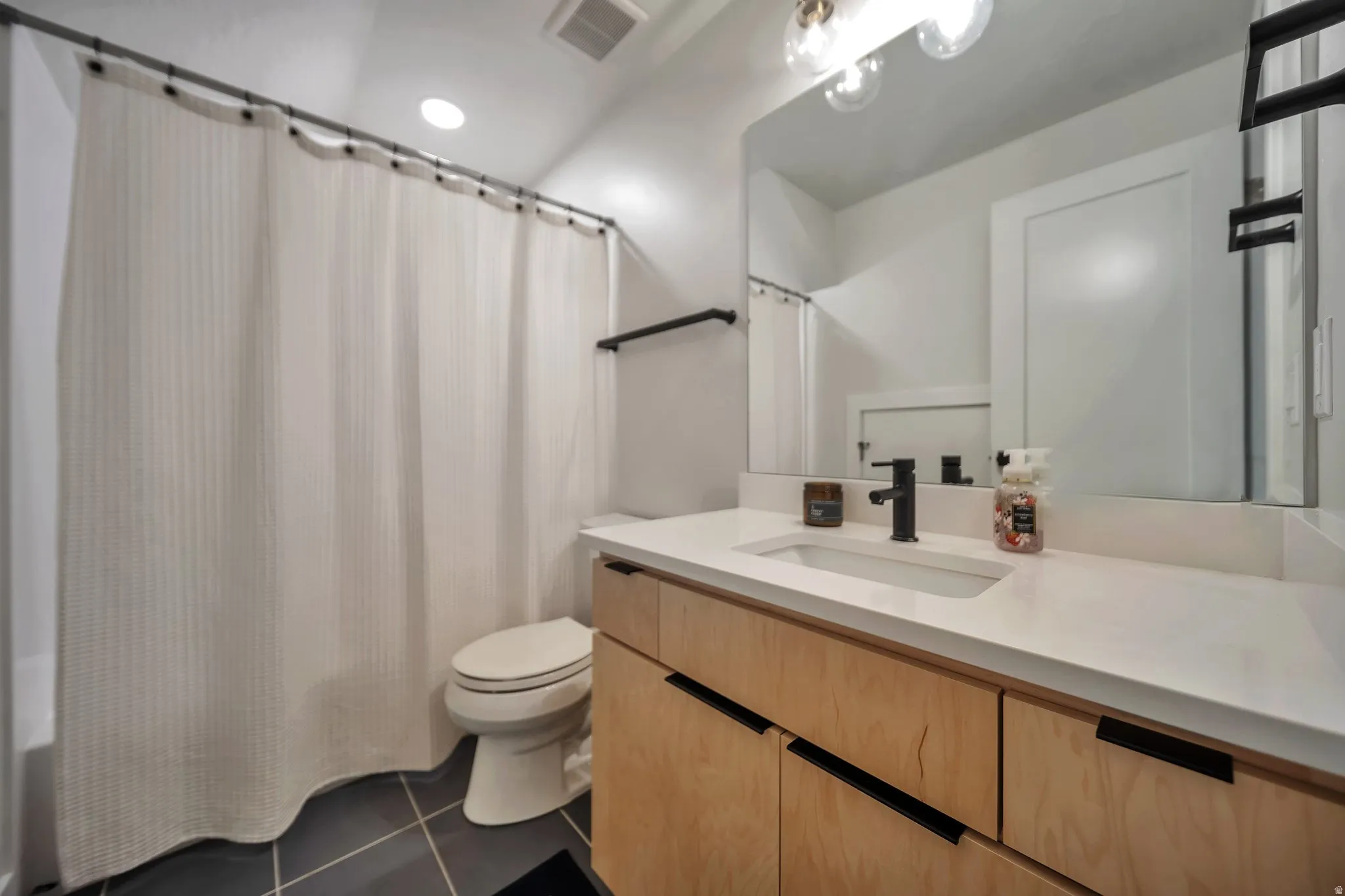 Bathroom featuring a light-toned wood vanity with dark hardware, a white countertop with an integrated rectangular sink, a matte black faucet, and a large wall mirror