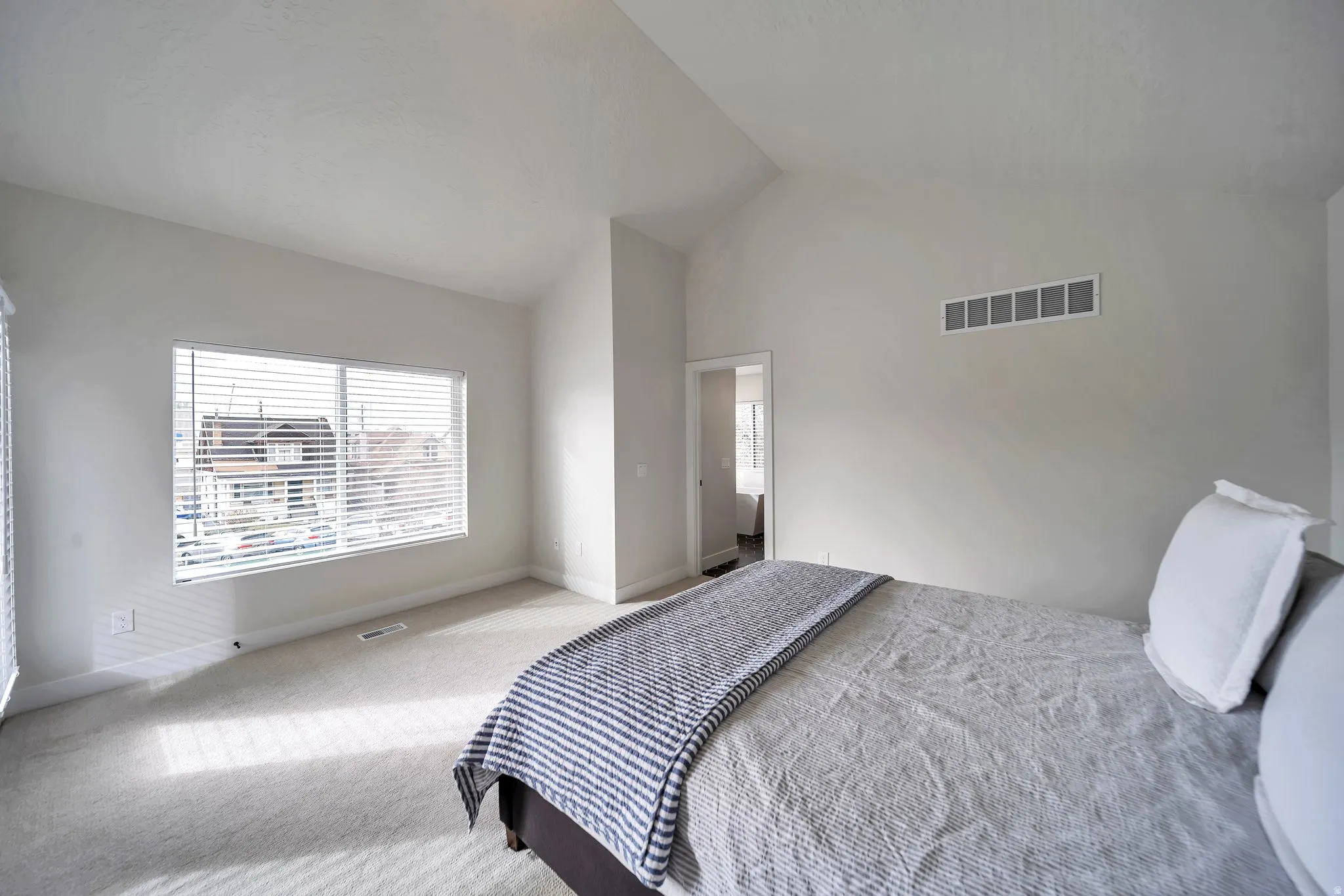 Bedroom featuring vaulted ceilings, light-colored carpet, a large window with blinds, and a neutral wall color