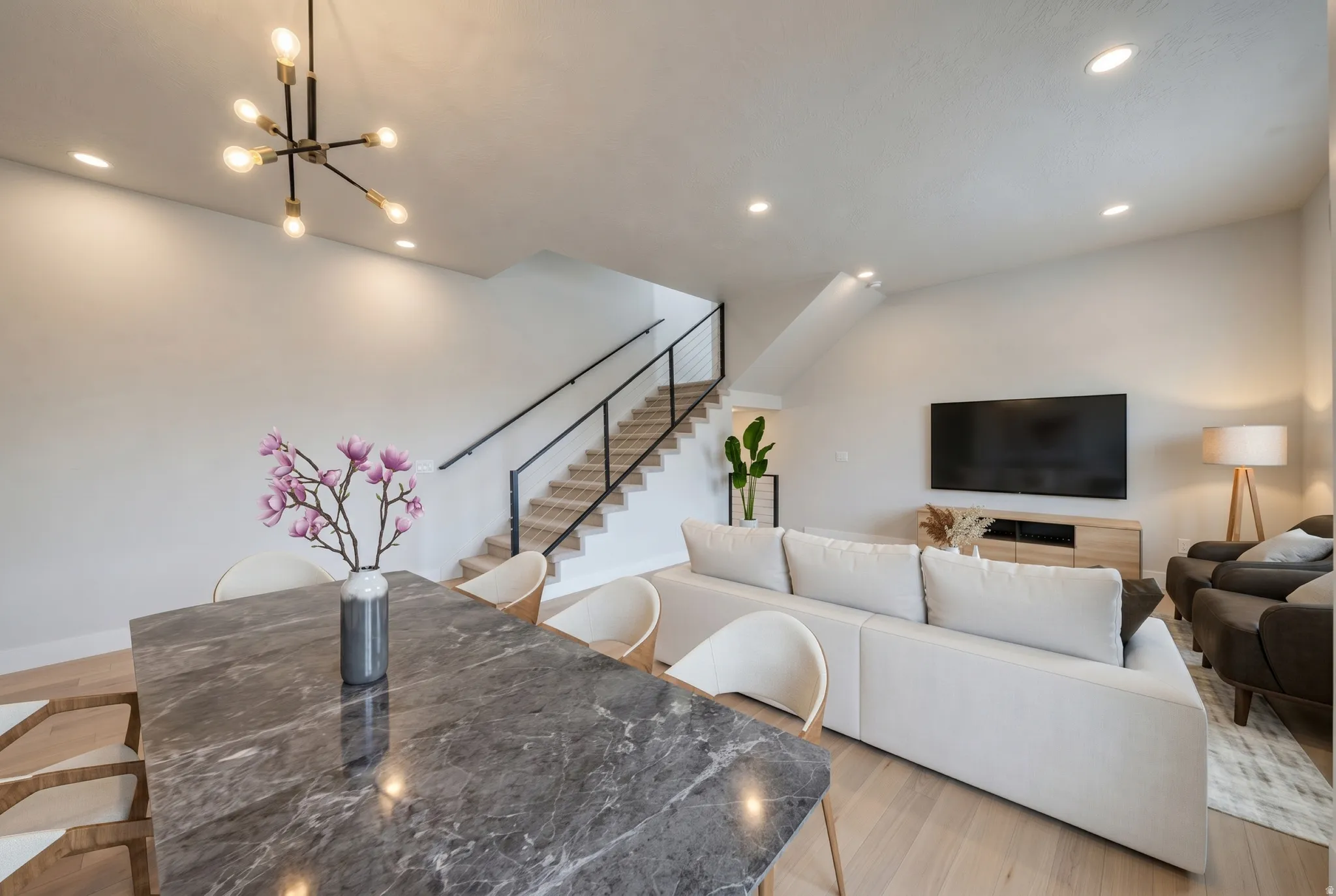 Open-concept living space featuring light wood-finish flooring, recessed lighting, and a modern staircase with black railings
