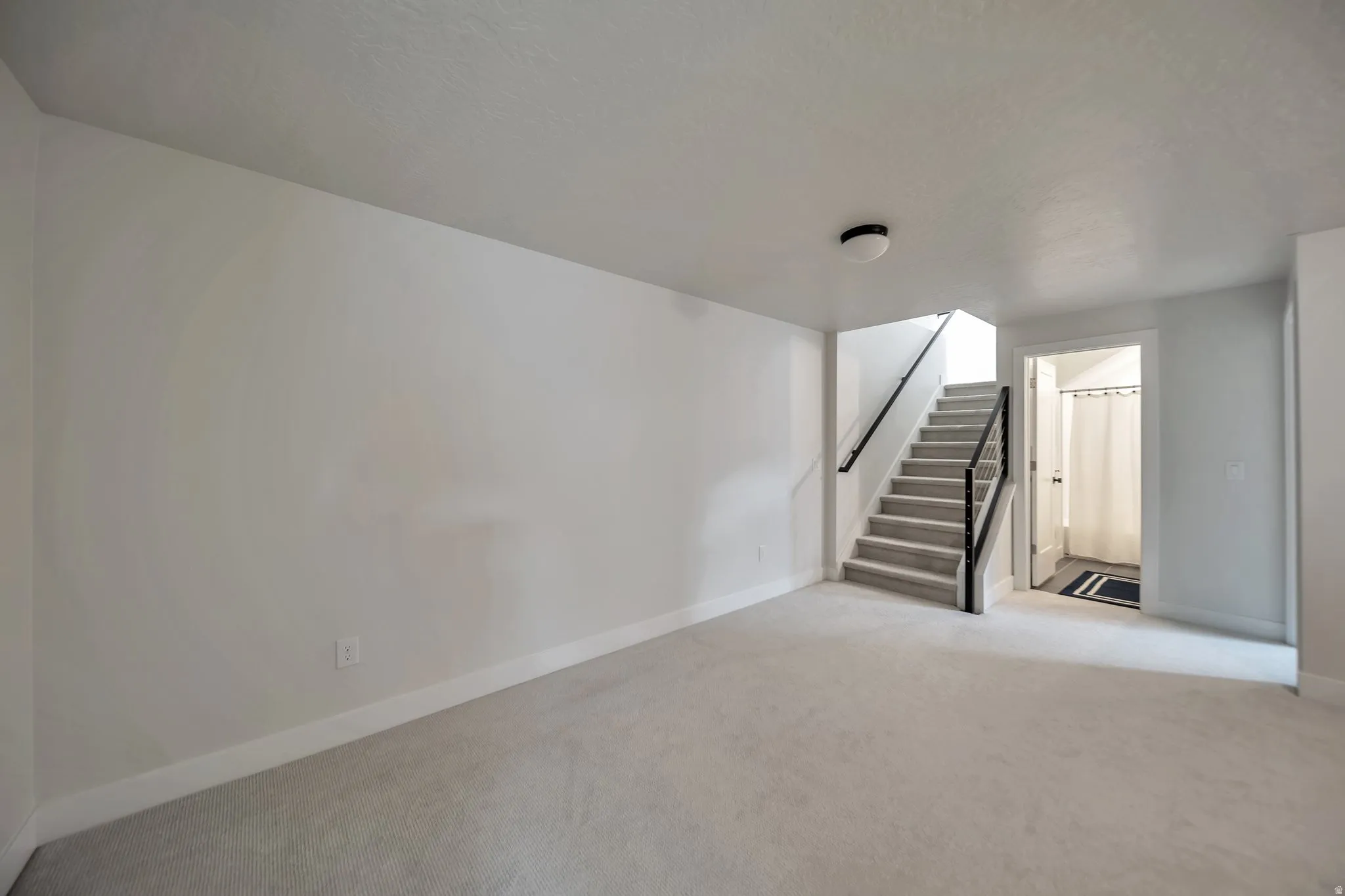 Carpeted room with a staircase featuring a black metal railing and a flush-mount light fixture