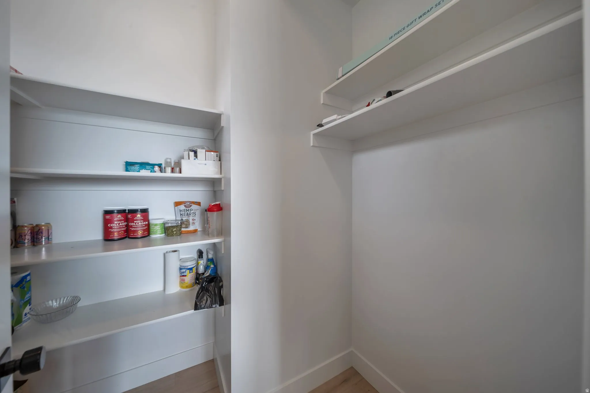 Walk-in pantry featuring white shelving, light wood-finish flooring, and white baseboards