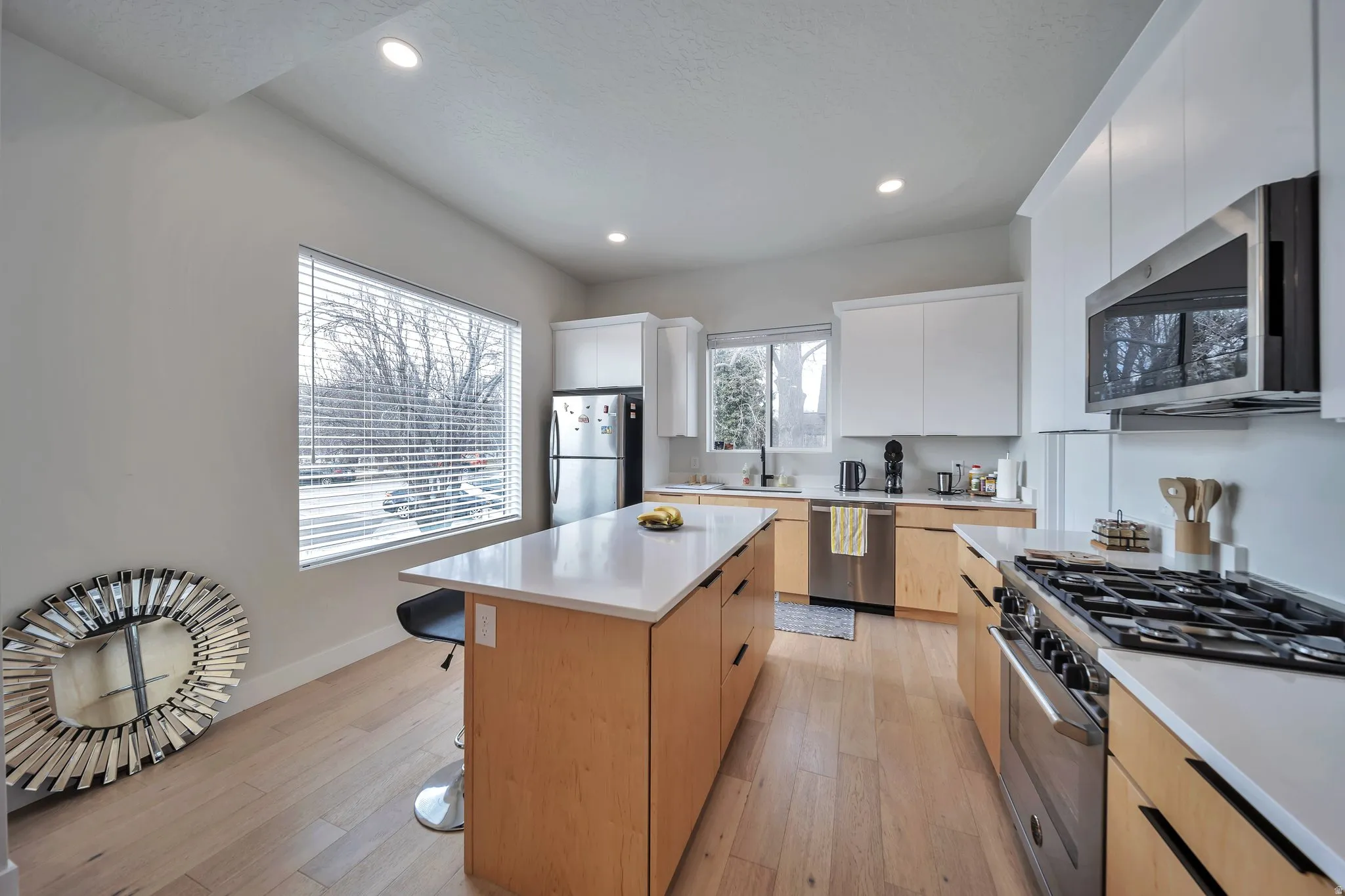 Contemporary kitchen featuring light wood-finish flooring, white flat-panel cabinetry, a light-toned island with integrated storage, and stainless steel appliances