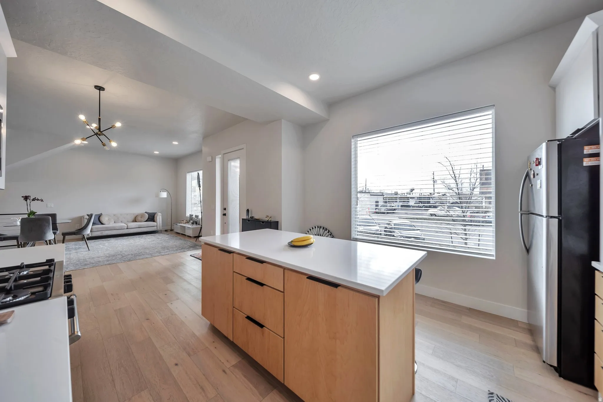 Kitchen with wood-finish flooring, a central island featuring a white countertop and natural wood cabinetry, and a large window with horizontal blinds