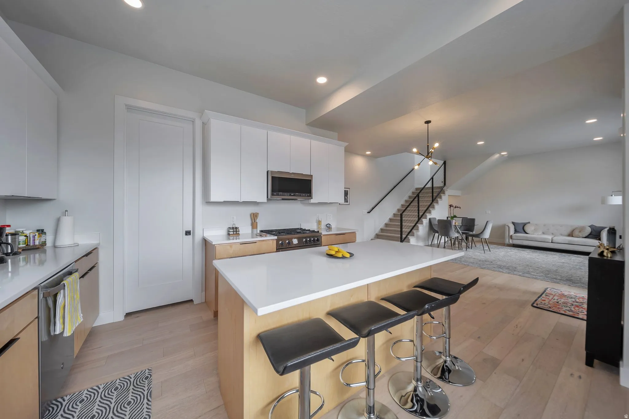 Open-concept kitchen featuring an island with counter seating, stainless steel appliances, light wood-finish flooring, and a contemporary staircase with black railings
