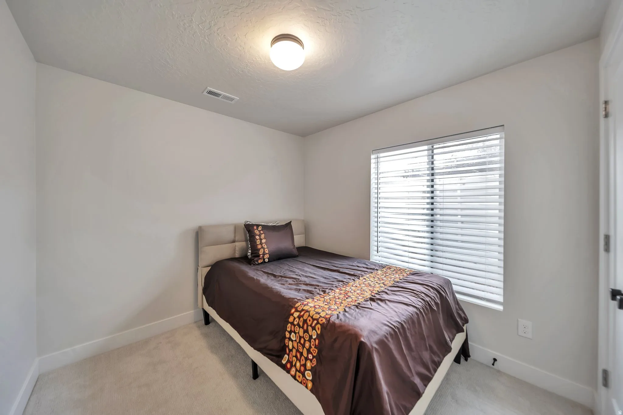 Bedroom featuring neutral wall paint, carpeted flooring, a window with horizontal blinds, a white door frame, and a flush-mount ceiling light