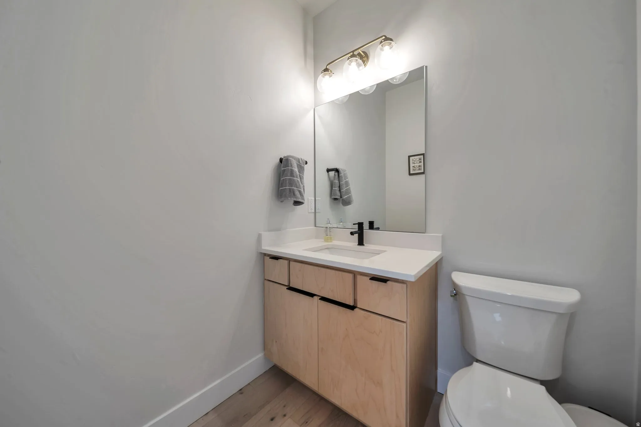 Powder room featuring a light wood-finish vanity with black hardware, white countertop, and rectangular sink