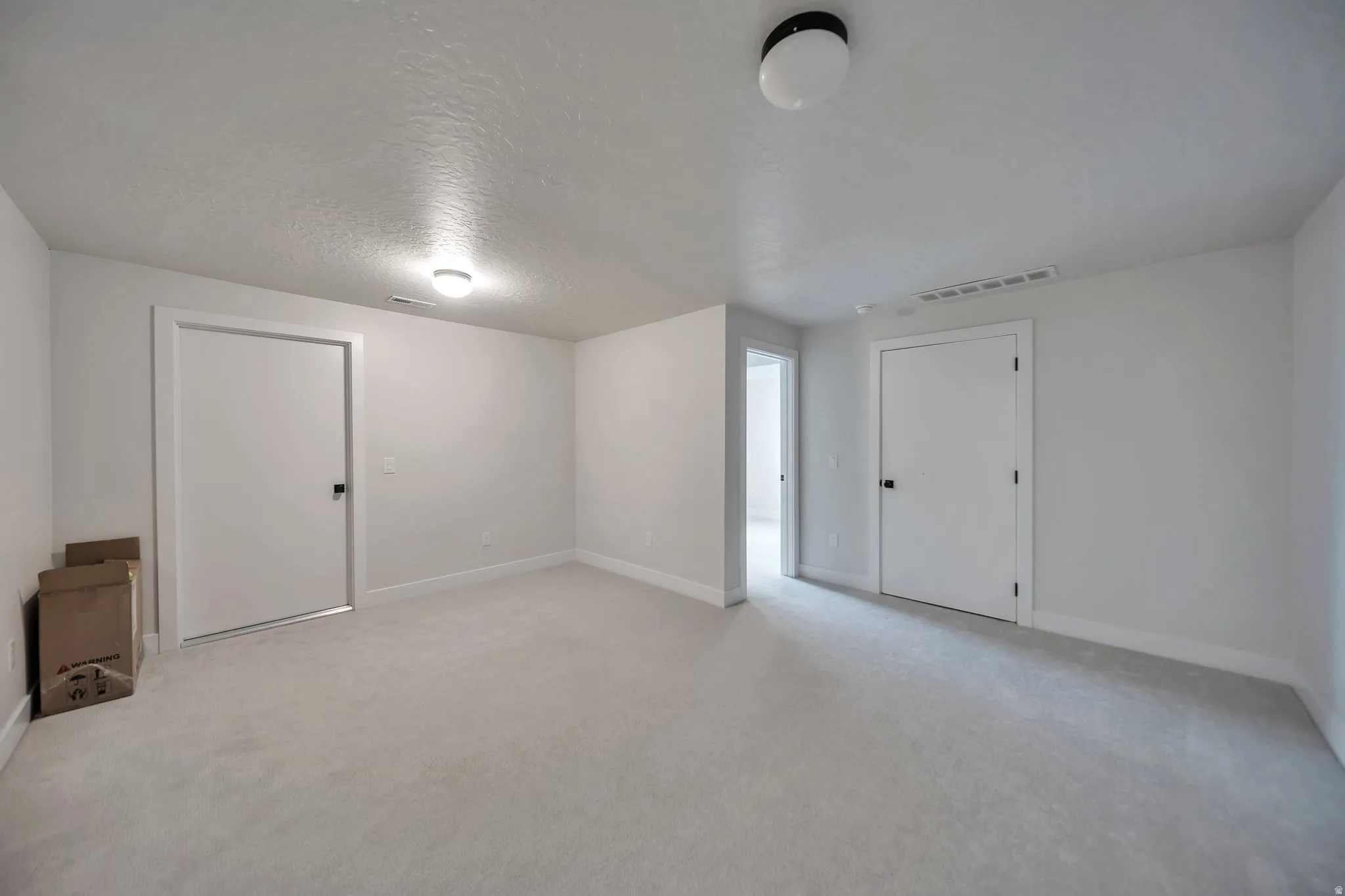Spacious room featuring light-toned carpet flooring, white walls, and white baseboards